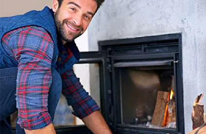 Eine lächelnde Person legt Holz in einen Kamin.